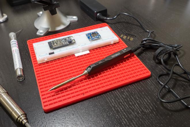 TS-100 smart soldering iron and power supply in work area.